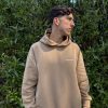 Joven con sudadera algodón orgánico marrón LUXXCORE mirando hacia un lado, frente a una vegetación frondosa.