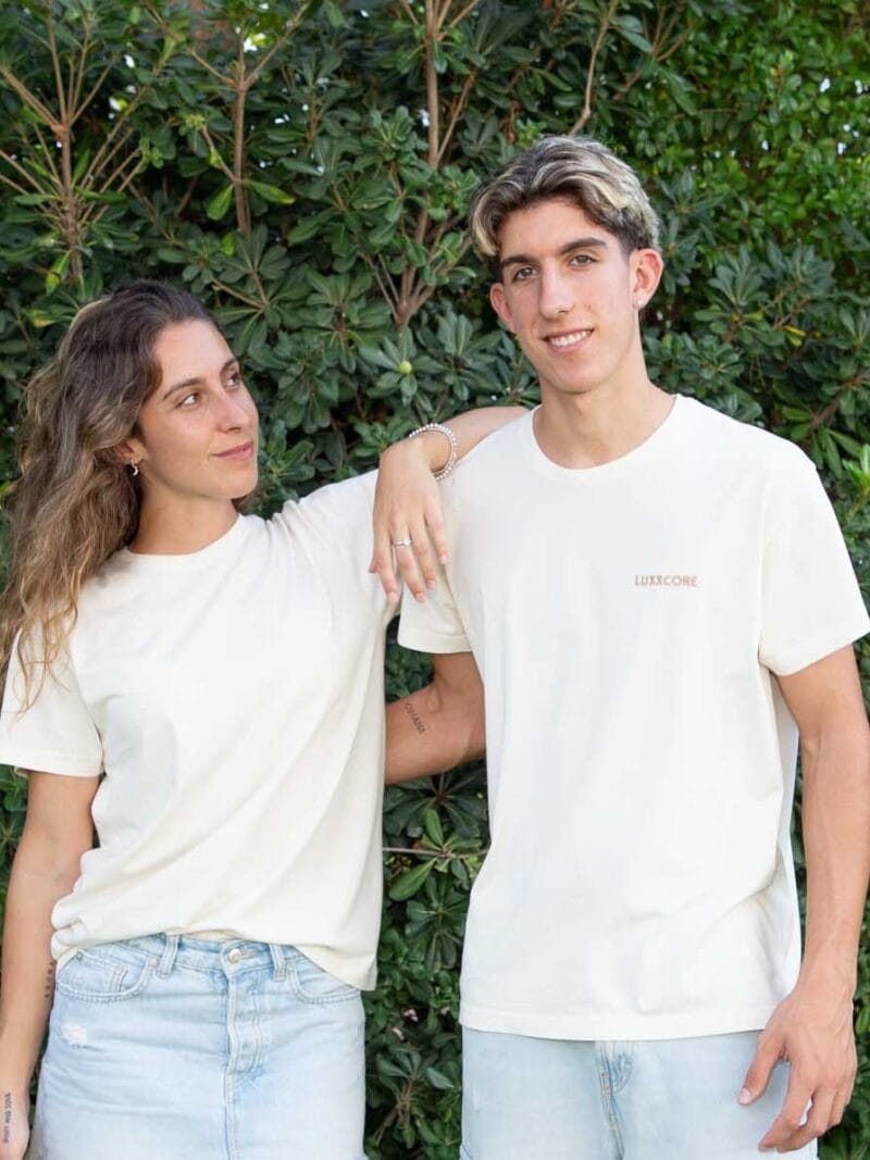 Hermana y hermano con camisetas LUXXCORE, él mira al frente, mientras su hermana lo mira con complicidad frente a un fondo verde de naturaleza.